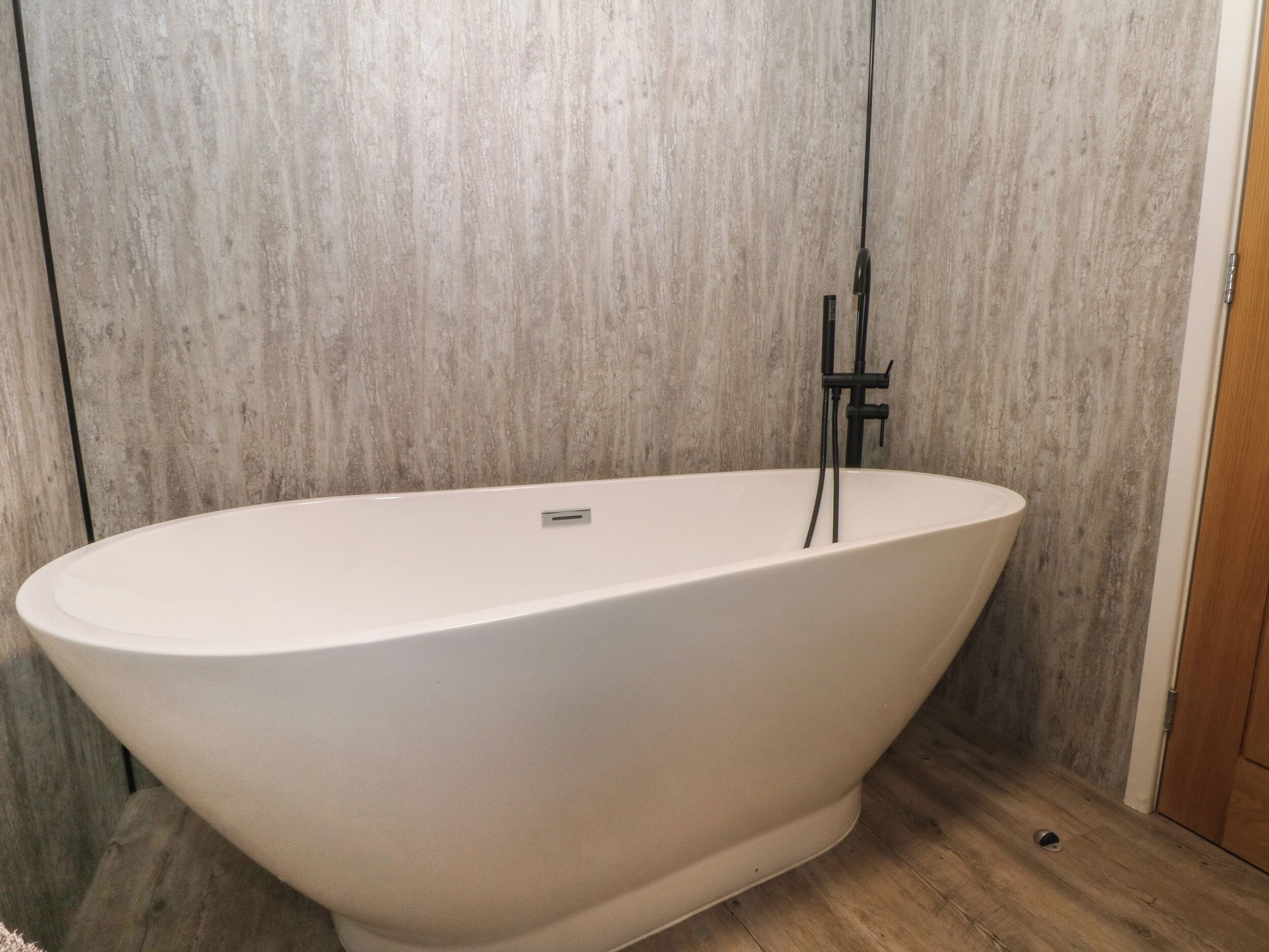 A freestanding bathtub in a bathroom with a wooden floor and a textured wall.