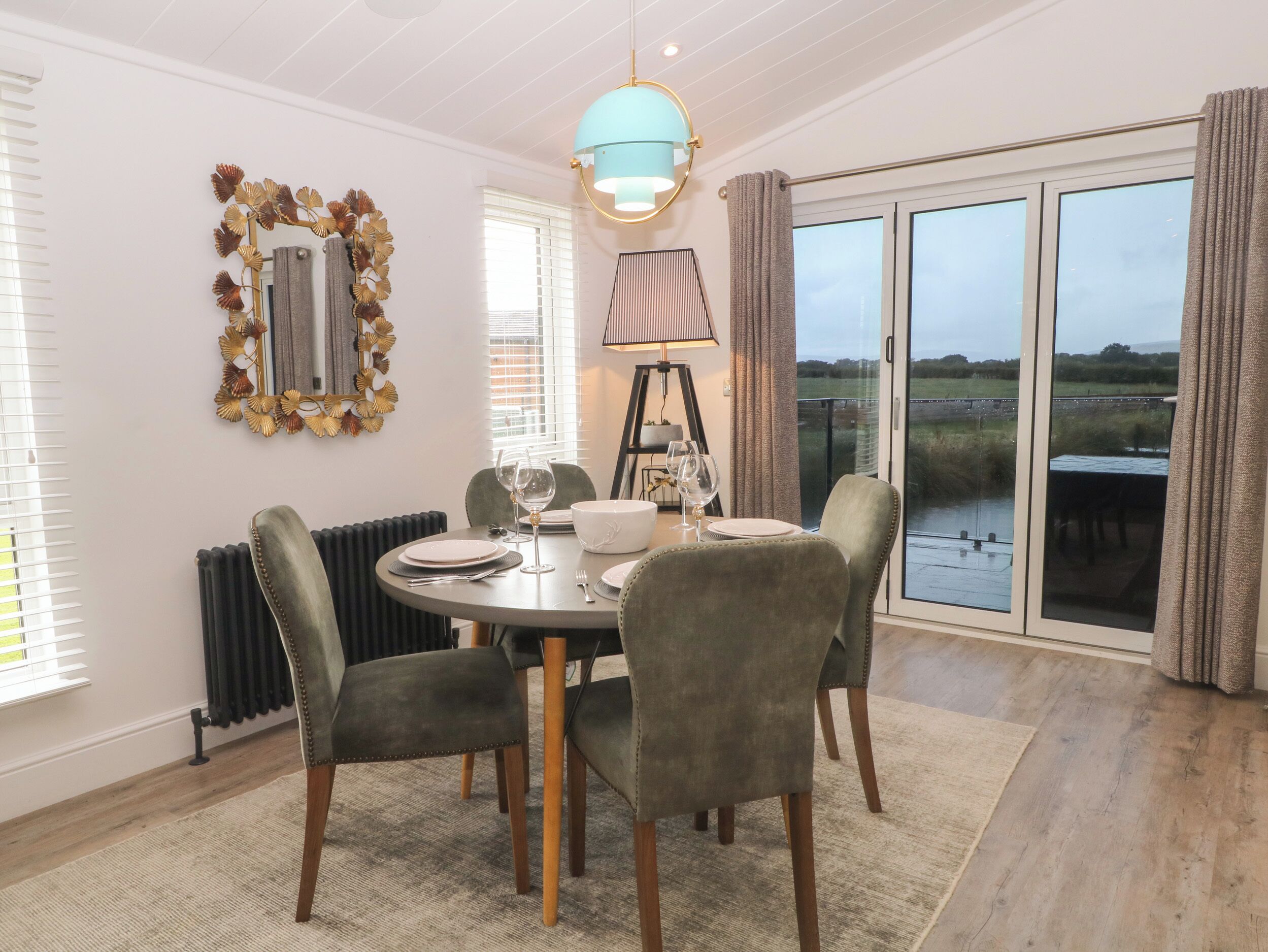 A dining area with a round table, four chairs, and a view of a lake through large windows.