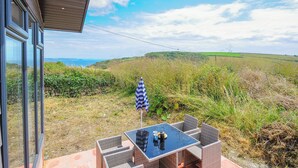 Un patio con mesa y sillas, con vista a un paisaje cubierto de hierba y una lejana vista del mar.