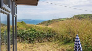 Vista desde una ventana que da a un paisaje costero con un muro de piedra y un paraguas.