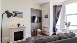 A modern living room with a fireplace, a flat-screen TV, a sofa, and a dining area with a table and chairs. - 6 Beach View @ Beaconsfield House (Bridlington)