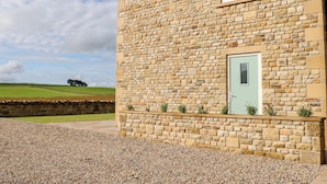 A stone building with a green door, a small window, and a gravel driveway. - Forestside View (Bishop Auckland)