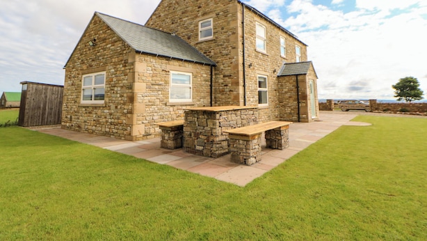 A stone house with a sloped roof, a front porch, and a well-maintained lawn. - Forestside View (Bishop Auckland)