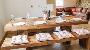 A dining area with a wooden table set for four, a clock on the wall, and a leather couch in the background. - Forestside View (Bishop Auckland)