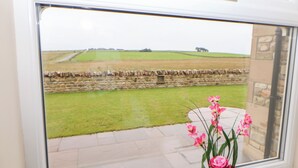 A view through a window of a stone wall, a grassy field, and a flower vase on a windowsill. - Forestside View (Bishop Auckland)
