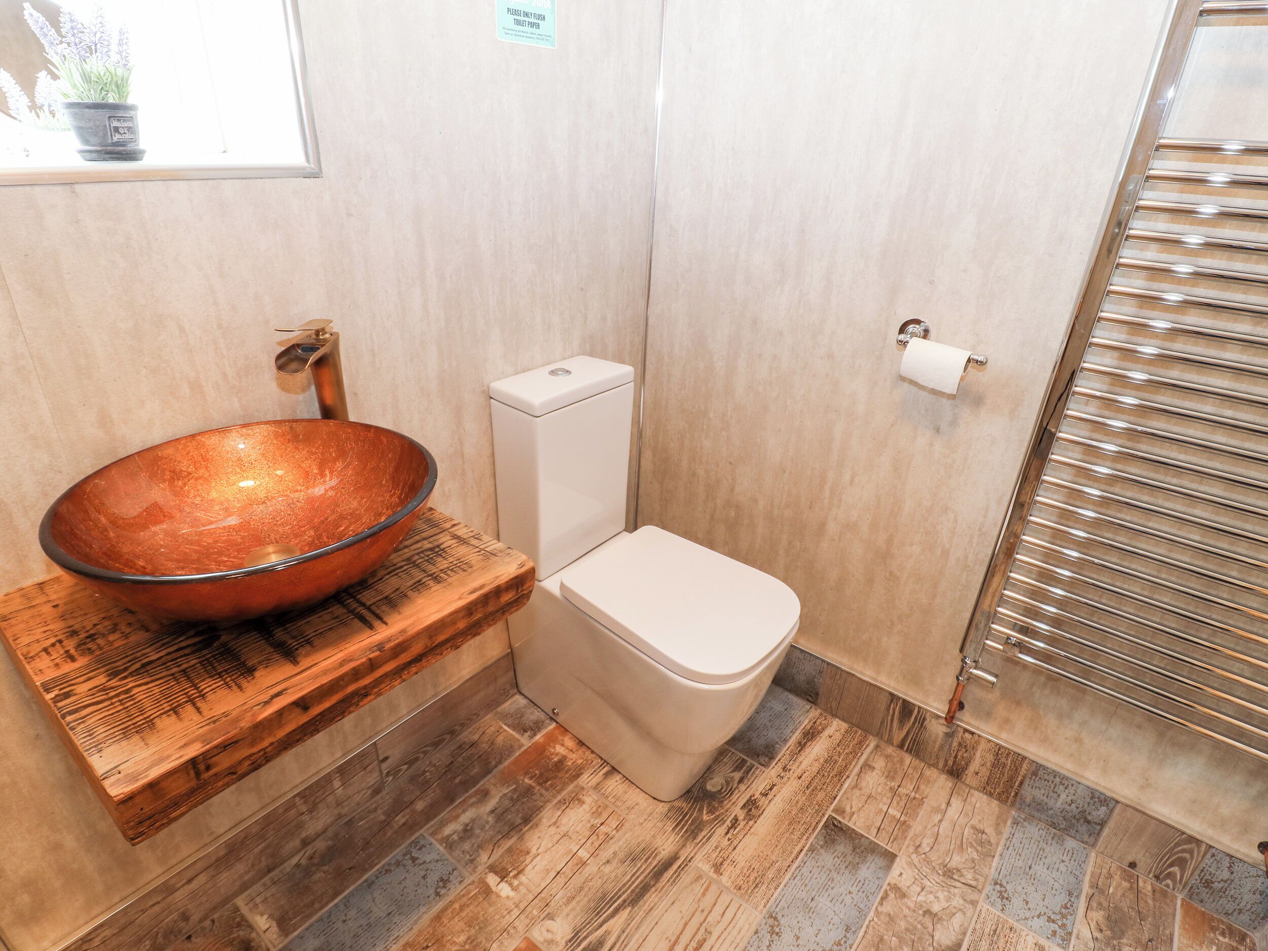 A bathroom with a wooden vanity, a copper bowl sink, a white toilet, and a shower with a glass door.