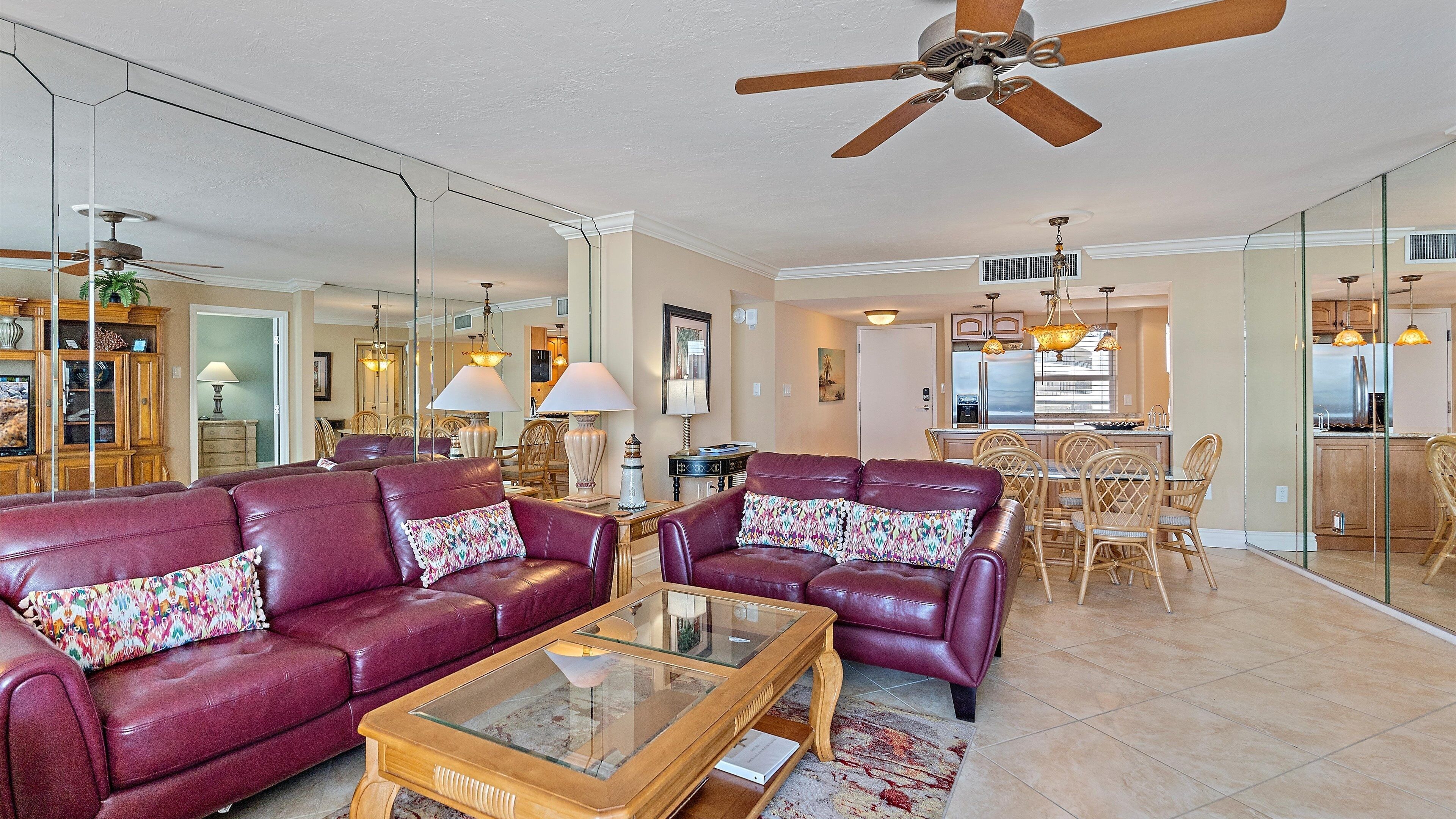 A spacious living room with leather sofas, a glass coffee table, and a ceiling fan.