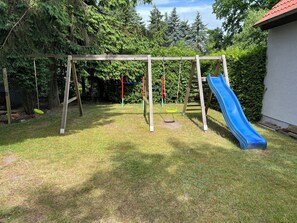 A backyard with a wooden swing set, a blue slide, and a fenced area.