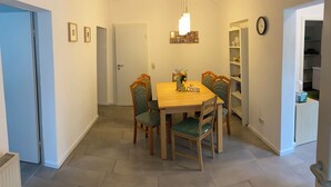 Uma área de refeições com mesa e cadeiras de madeira, luminária pendente e uma estante de livros.