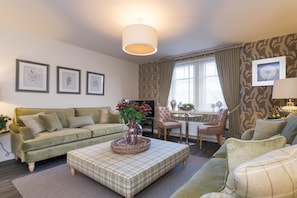 Relax in this inviting living room with a sofa, ottoman, and TV, surrounded by framed prints and a stylish lamp.