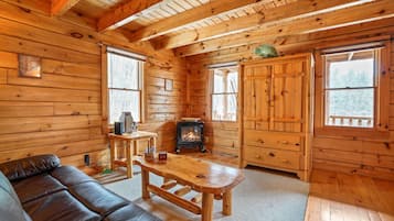 Un intérieur de chalet chaleureux avec un plancher en bois, un canapé en cuir, une table en bois, une cheminée et de grandes fenêtres.