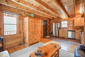 A log cabin interior with a kitchen, wooden cabinets, a dining table, and a fireplace.