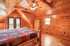 Une chambre aménagée dans un chalet en rondins, avec un lit, des murs en bois, un ventilateur de plafond et une fenêtre.