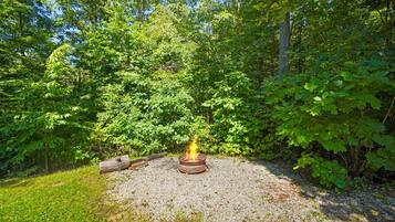 Un terrain de camping avec un foyer entouré de gravier, d’arbres et de verdure.
