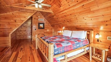 Une chambre confortable dans un chalet en rondins, avec un lit en bois, un ventilateur de plafond et un escalier menant à un étage supérieur.