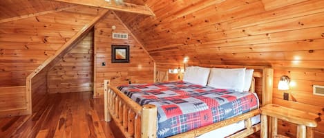 Acogedor dormitorio de cabaña de troncos con cama de madera, ventilador de techo y escalera que conduce a un nivel superior.