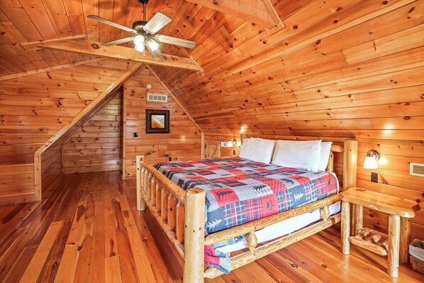 A cozy log cabin bedroom with a wooden bed, a ceiling fan, and a staircase leading to an upper level.