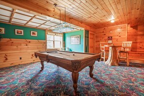 Ein Billardtisch in einem Raum mit Holzwänden und einem farbenfrohen Teppich.