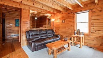 L’intérieur d’un chalet en bois est aménagé avec un canapé en cuir, une table basse en bois et une petite table en bois sur laquelle se trouve une lampe.