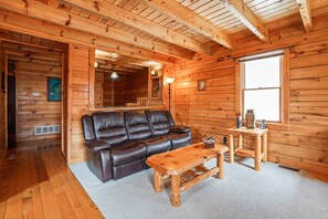 A wooden cabin interior with a leather sofa, a wooden coffee table, and a small wooden table with a lamp.