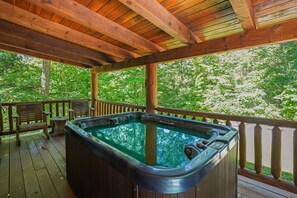 A wooden deck with a hot tub, wooden benches, and a view of a forest. - The Hemlock | Hocking Hills, Romantic, Hot Tub (Rockbridge)