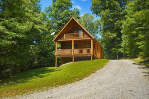 A wooden cabin with a balcony, surrounded by trees and a gravel path. - The Hemlock | Hocking Hills, Romantic, Hot Tub (Rockbridge)