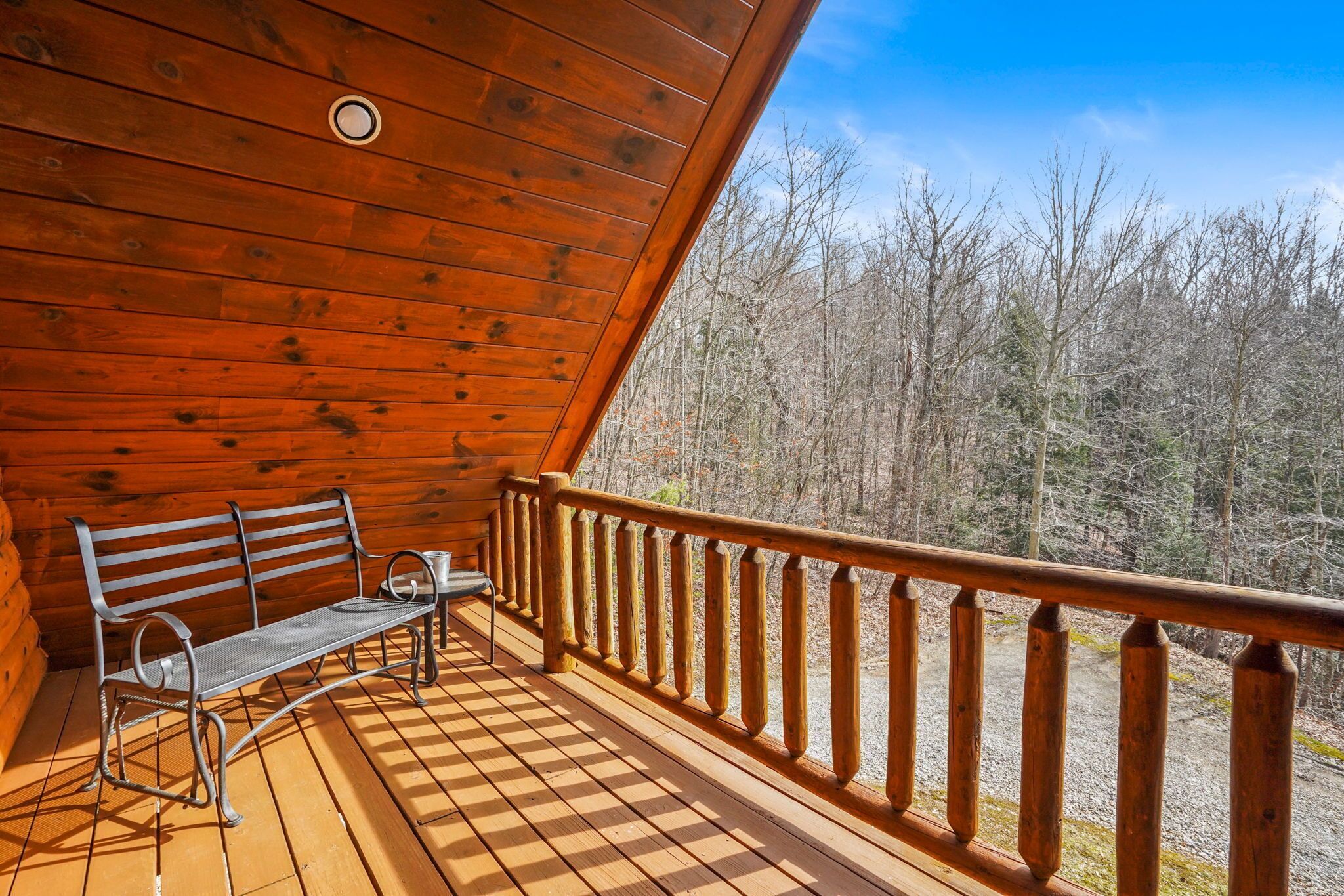 Une terrasse en bois avec un banc et une table, donnant sur une zone boisée.