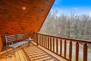 A wooden deck with a bench and table, overlooking a forested area.