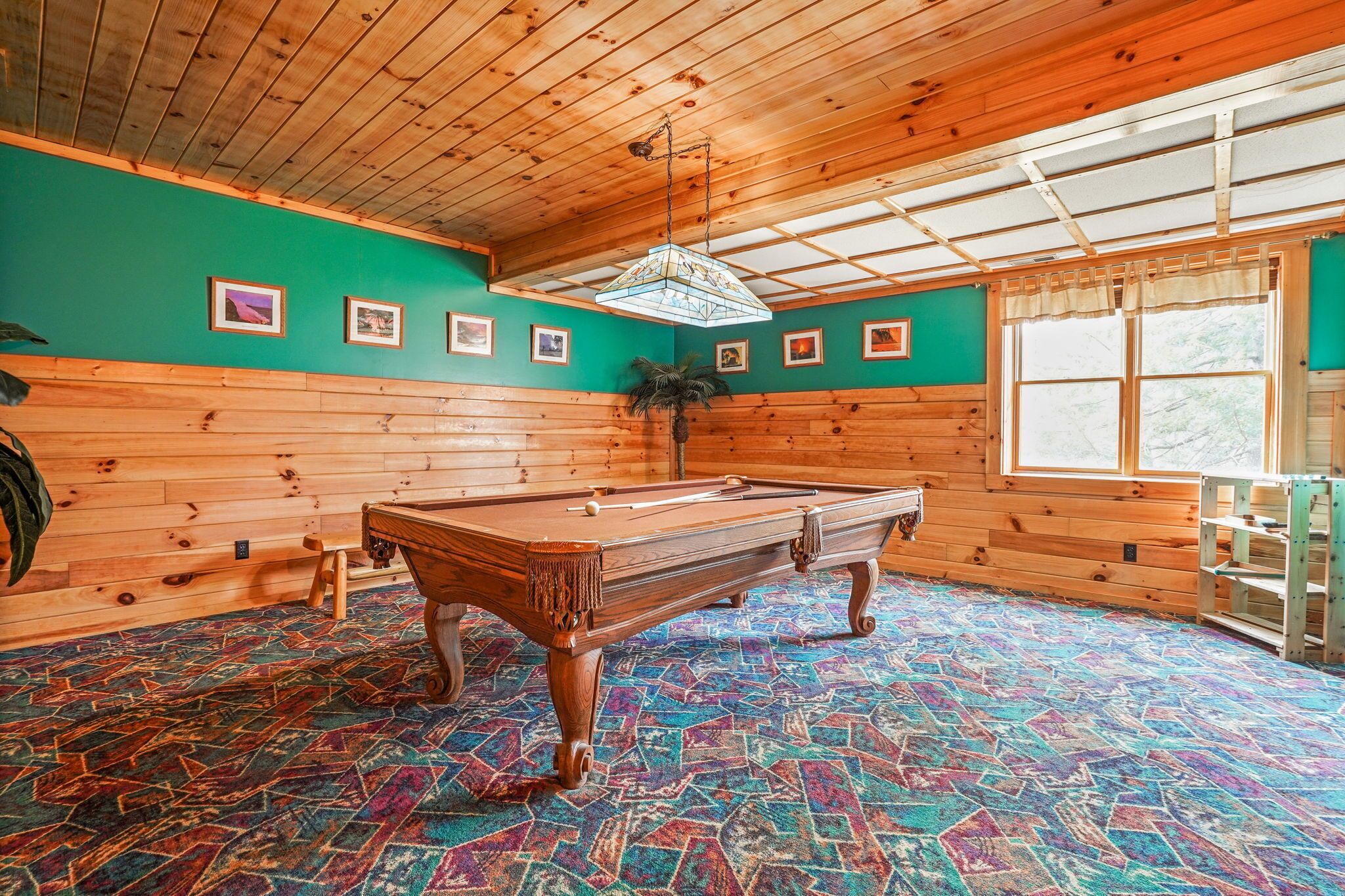 A pool table in a room with wooden walls and a colorful carpet.