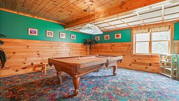 A pool table in a room with wooden walls and a colorful carpet.