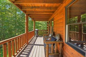 Une terrasse en bois avec une rambarde, un banc et une fenêtre équipée de stores.