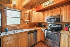 Une cuisine rustique aménagée dans une cabane en bois, équipée d’un lave-vaisselle, d’un four et d’un four à micro-ondes en acier inoxydable.