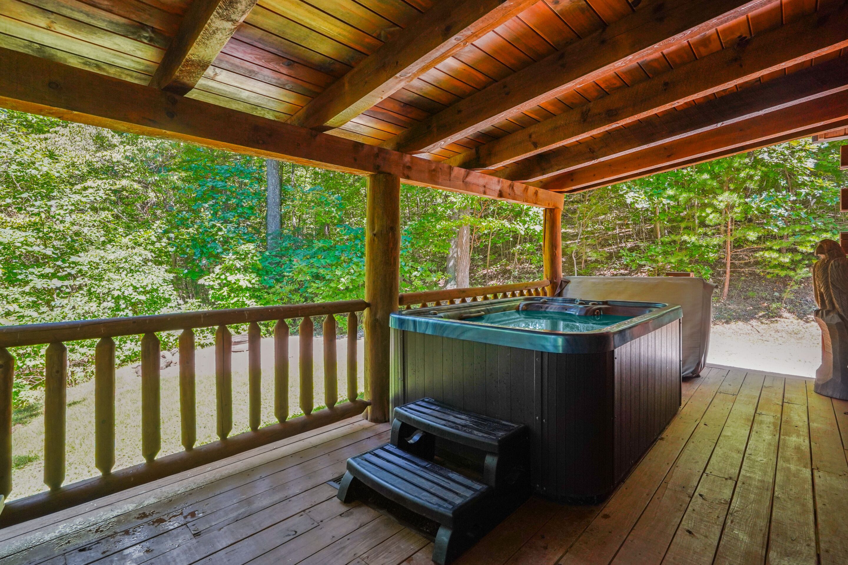 Una terraza de madera con un jacuzzi y un banco, rodeada de árboles.