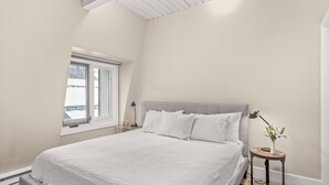 A bedroom with a bed, a nightstand, a lamp, and a window. - Chateau Dumont 16 (Aspen)