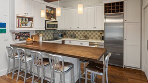 A modern kitchen with white cabinetry, a wooden island, stainless steel appliances, and hanging pendant lights. - Chateau Dumont 16 (Aspen)