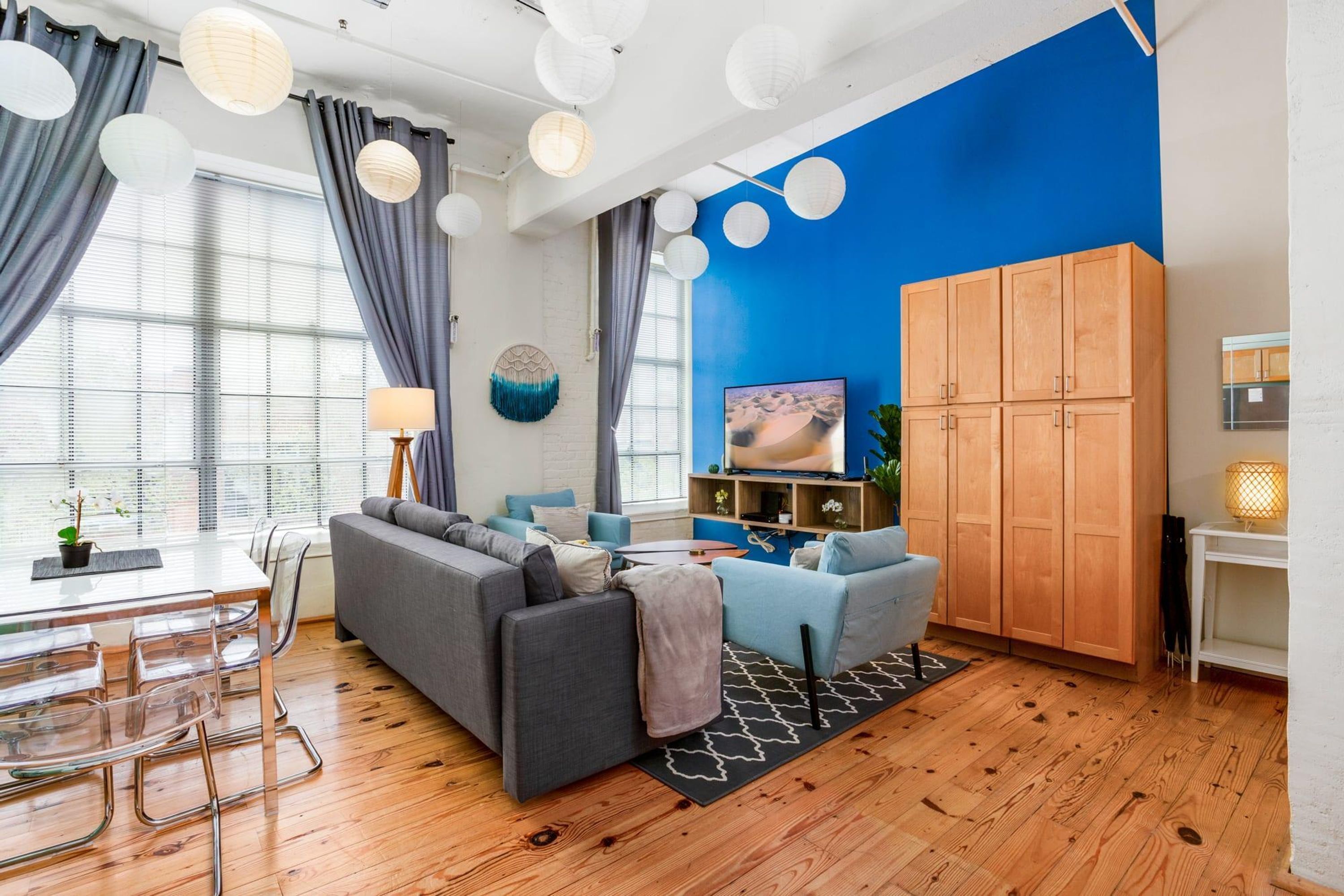 A modern living room with a grey sofa, blue armchairs, wooden cabinets, and a TV on a wooden stand.