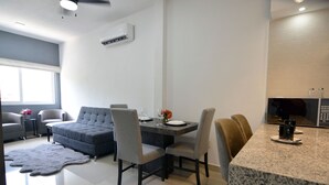A modern living room with a grey sofa, a dining table with chairs, and a kitchen area with a granite countertop and microwave. - Convenient Condo near Gourmet District + Pool (Puerto Vallarta)