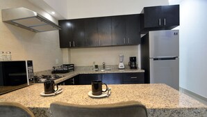 A modern kitchen with dark cabinets, granite countertops, a built-in stove, a coffee maker, and a refrigerator. - Convenient Condo near Gourmet District + Pool (Puerto Vallarta)