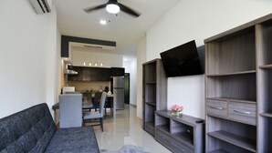 A modern living room with a grey sofa, a coffee table, and a grey rug. There is a TV mounted on the wall, a ceiling fan, and a kitchen area in the background. - Convenient Condo near Gourmet District + Pool (Puerto Vallarta)