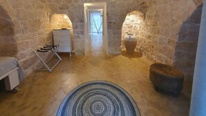 A stone-walled room with a bed, a drying rack, a large vase, and a circular rug. - Trullo Oscar (Ceglie Messapica)