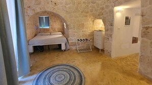 A stone-walled room with a bed, a small table, and a lamp. - Trullo Oscar (Ceglie Messapica)