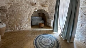 A stone-walled room with a sofa, a small rug, and a window with curtains. - Trullo Oscar (Ceglie Messapica)