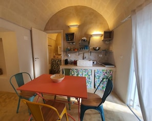 Cocina compacta con horno integrado, un lavamanos y una pequeña encimera. En primer plano, una mesa con sillas.