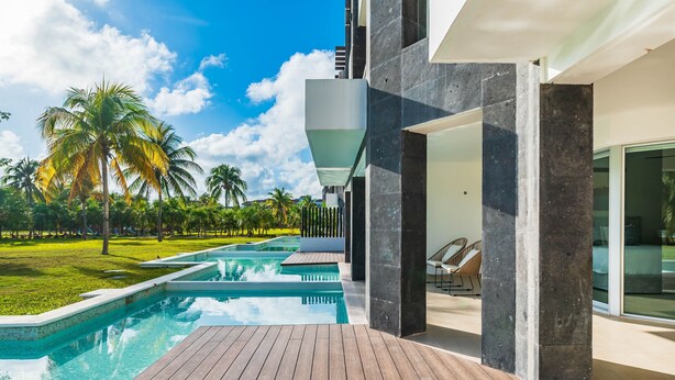 A modern pool area with a wooden deck, a clear blue pool, and palm trees in the background. - Casa Bellisima ! 2 bedroom swim up 2 Apts by RedAwning (Playa del Carmen)