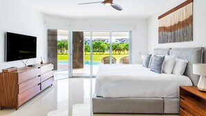 A modern bedroom with a large bed, a flat-screen TV, a wooden dresser, and a ceiling fan. - Casa Bellisima ! 2 bedroom swim up 2 Apts by RedAwning (Playa del Carmen)