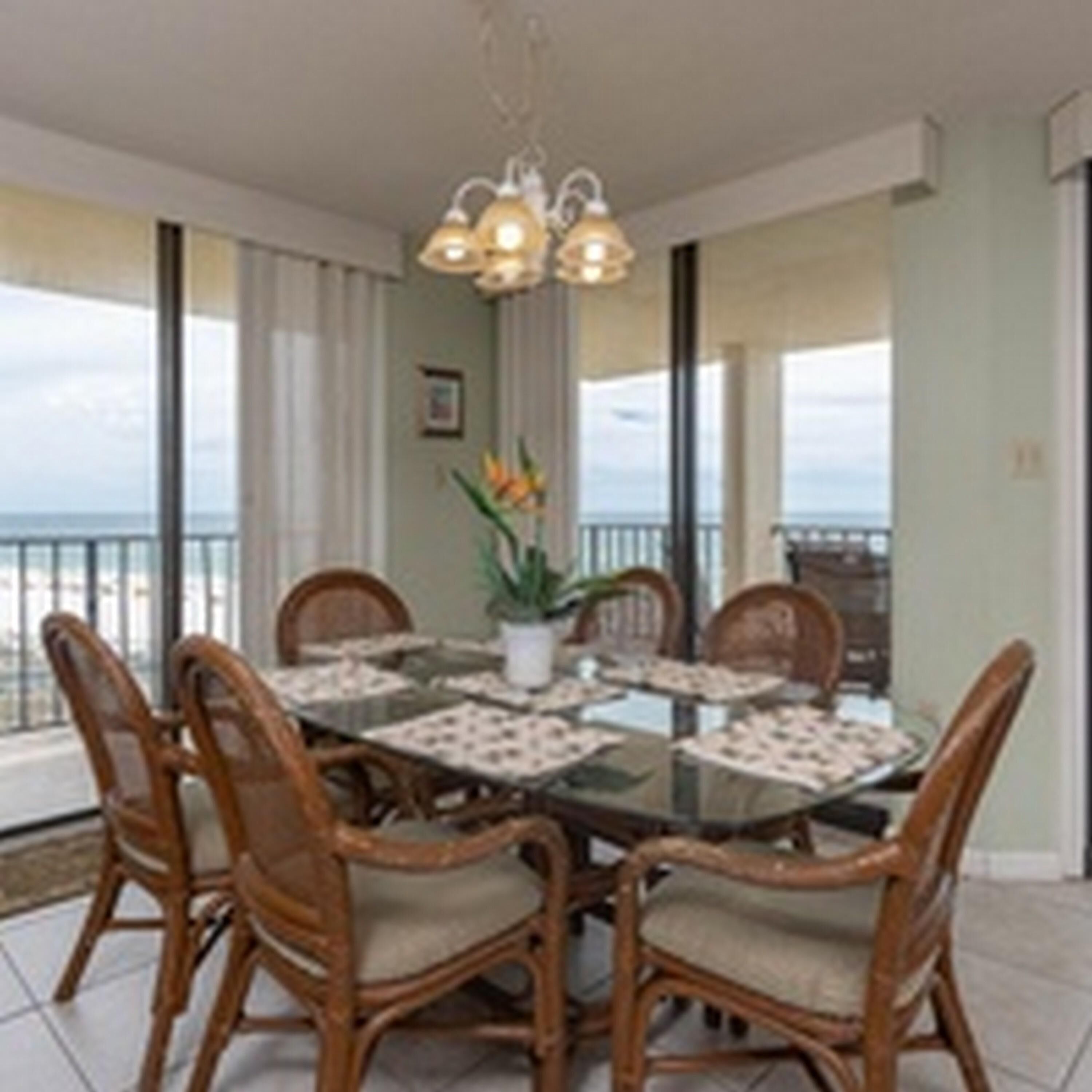 A dining area with a glass table, wicker chairs, and a ceiling light fixture.
