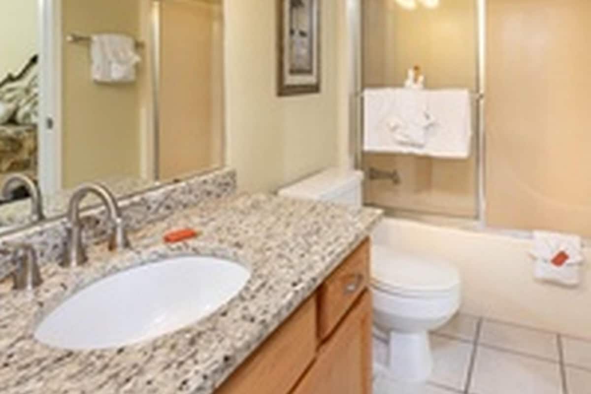 A bathroom with a granite countertop, a sink, a toilet, and a shower area.
