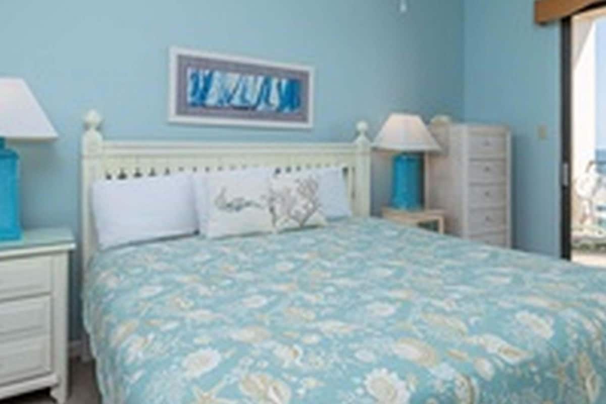 Un dormitorio con una cama, dos mesitas de noche, un aparador y un cuadro en la pared.
