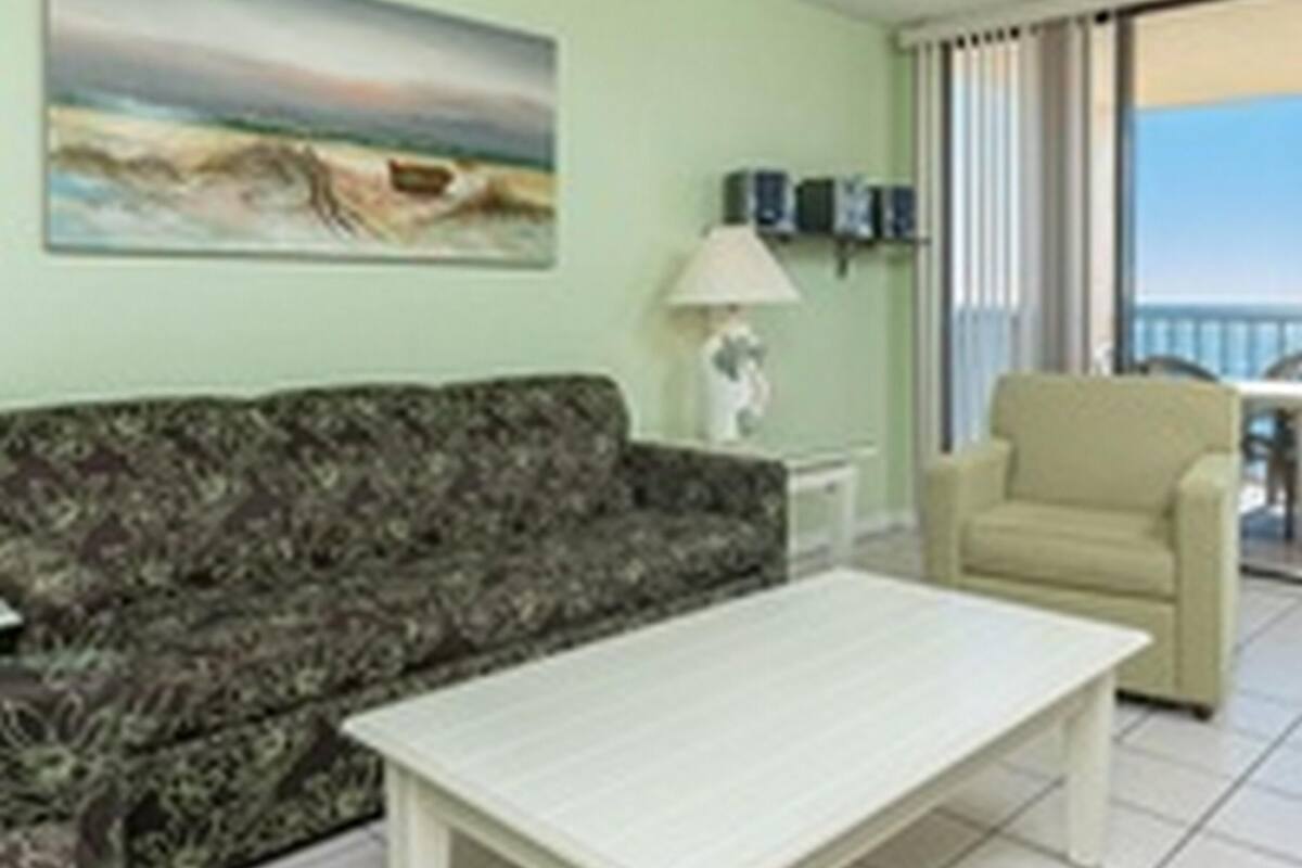 Una sala de estar con un sofá estampado, una mesa de centro blanca, una lámpara y un cuadro en la pared.