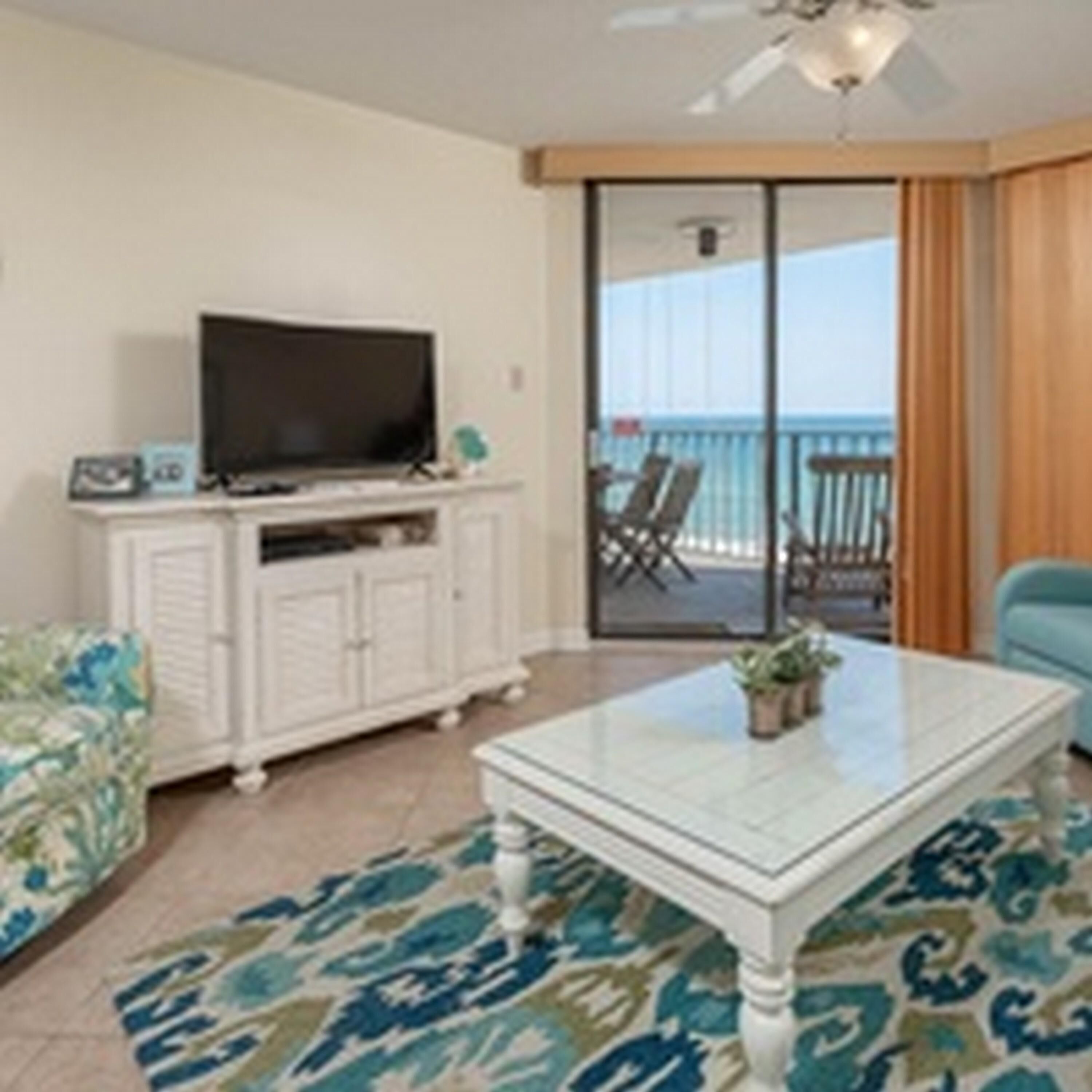 A living room with a white cabinet, a flat-screen TV, a glass coffee table, and a patterned rug.